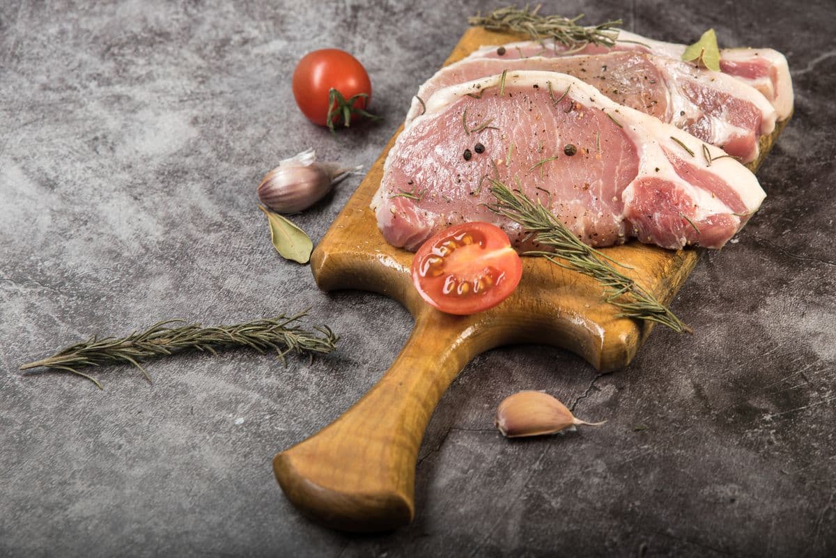 Fresh raw pork chops with rosemary and peppercorns on a cutting board