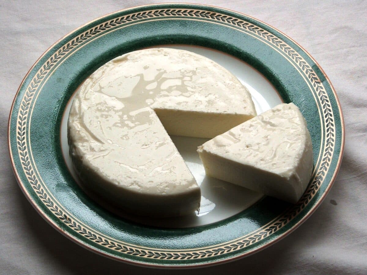 Fresh queso fresco wheel with a cut wedge on a plate